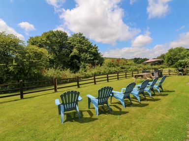 A garden with a row of blue chairs on grass and a picnic table with an umbrella at Apple Barn in South Molton