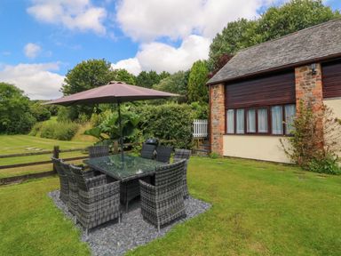 An outdoor dining area with a glass table and umbrella on a lawn outside a house at Apple Barn in South Molton