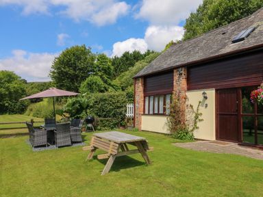 A backyard with a wooden picnic table and a dining set with an umbrella next to a building at Apple Barn in South Molton