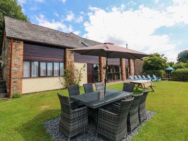 Outdoor patio dining table with umbrella and chairs on grass next to a stone and brick building at Apple Barn in South Molton
