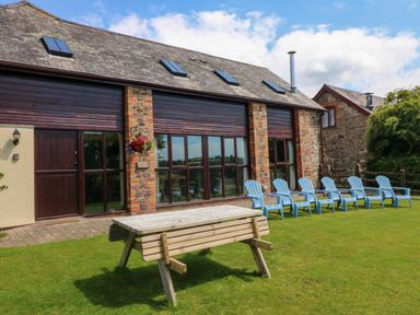 A grassy outdoor area with a wooden picnic table and six blue chairs in front of a stone and wood building at Apple Barn in South Molton