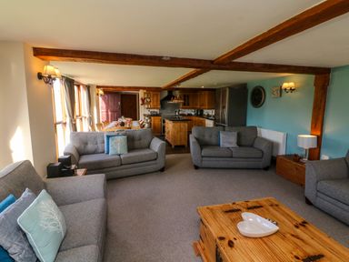 A living room with gray sofas a wooden coffee table and an open kitchen and dining area in the background at Apple Barn in South Molton