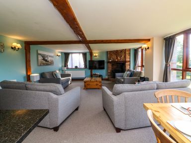 A living room with grey sofas, a wooden coffee table, a television, and a dining table with chairs at Apple Barn in South Molton