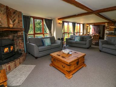A living room with grey sofas a wooden coffee table a brick fireplace and large windows at Apple Barn in South Molton