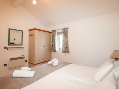 A bedroom with a bed with white linens a wardrobe a window with curtains and a wall heater at Beside the Sea in Eype
