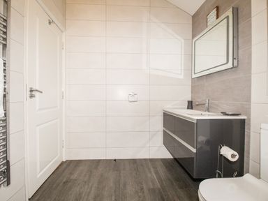 A bathroom with a sink cabinet mirror toilet door towel radiator and tiled walls at Beside the Sea in Eype