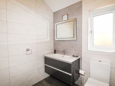 A bathroom with a wall-mounted sink cabinet mirror above the sink and a toilet beside a window at Beside the Sea in Eype