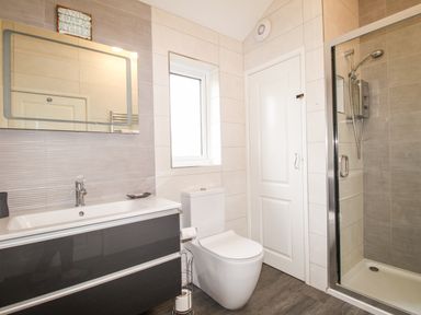 A bathroom with a sink vanity, toilet, shower enclosure, and a window at Beside the Sea in Eype