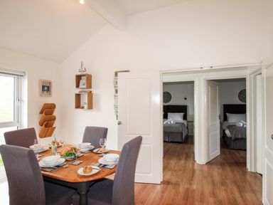 A dining area with a wooden table set for four and two bedrooms visible through open doors at Beside the Sea in Eype