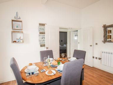 A dining room with a wooden table set for four with chairs and decorated walls at Beside the Sea in Eype