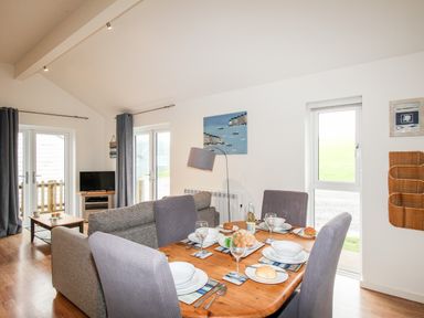 A dining table set for four next to a living area with sofas and a TV at Beside the Sea in Eype