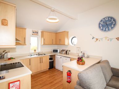 A kitchen with wooden cabinets a countertop sofa a wall clock and a fire extinguisher at Beside the Sea in Eype