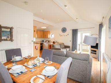 An open plan living room and kitchen with a dining table set with plates and glasses at Beside the Sea in Eype