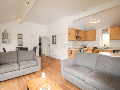 An open plan living room and kitchen with two grey sofas a wooden floor and dining table at Beside the Sea in Eype