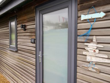 An exterior wooden wall with a frosted glass door and a small window beside it at Beside the Sea in Eype