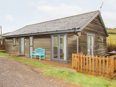 A wooden cabin with a blue bench outside and a small fenced deck at Beside the Sea in Eype