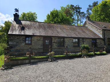 A stone cottage with wooden windows and a gravel driveway at Ty Barcud in Llanfair Clydogau