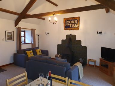 A living room with two sofas a wood stove a television and a dining table at Ty Barcud in Llanfair Clydogau