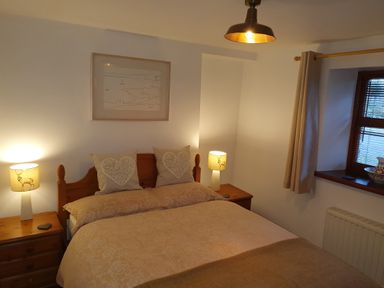 A bedroom with a double bed two bedside tables with lamps and a window with curtains at Ty Barcud in Llanfair Clydogau