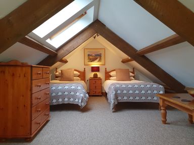 An attic bedroom with two single beds a wooden dresser a wooden bedside table with a lamp and a painting on the wall at Ty Barcud in Llanfair Clydogau