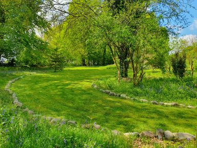 A grass pathway bordered by stones with trees and plants on both sides at Ty Barcud in Llanfair Clydogau