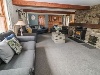A living room with grey sofas a wooden coffee table a stone fireplace and wooden beams at Hazel Barn in North Molton