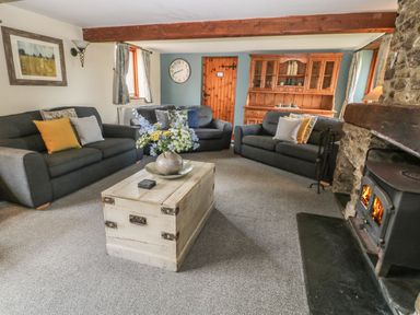 A living room with three sofas a wooden coffee table flowers on table a wood burning stove and a wooden cabinet at Hazel Barn in North Molton