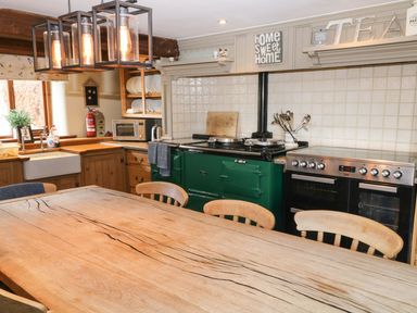 A kitchen with a wooden dining table and chairs a green stove a stainless steel oven white tiled backsplash and wooden cabinets at Hazel Barn in North Molton
