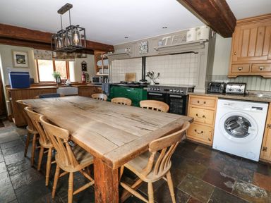 A kitchen with a large wooden dining table and chairs a washing machine and oven at Hazel Barn in North Molton