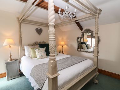 A bedroom with a four poster bed floral cushions bedside tables with lamps and a decorative mirror at Hazel Barn in North Molton