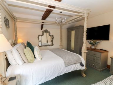 A bedroom with a four-poster bed pillows and a chandelier a wardrobe and a dresser with a vase and flowers at Hazel Barn in North Molton