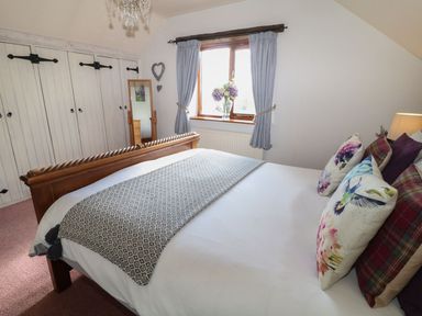 A bedroom with a wooden bed frame and decorative pillows next to a window with blue curtains at Hazel Barn in North Molton