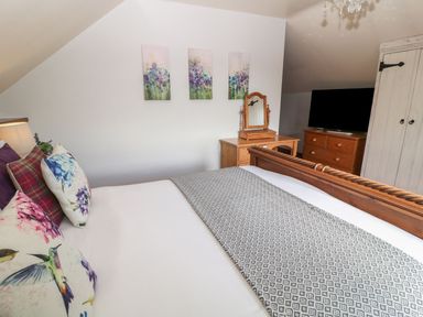 A bedroom with a wooden bed a dresser with a mirror a chest of drawers and a television at Hazel Barn in North Molton
