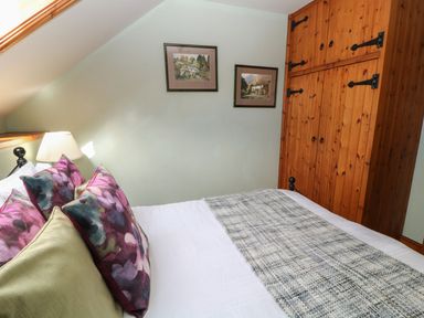 A bedroom with a bed, pillows, a lamp, framed pictures on the wall, and a wooden wardrobe at Hazel Barn in North Molton