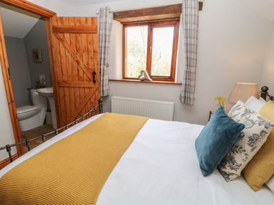 A bedroom with a bed next to a window and a door leading to a bathroom at Hazel Barn in North Molton