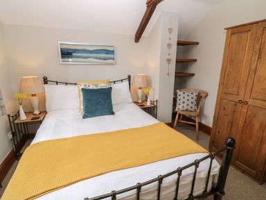 A bedroom with a double bed yellow throw pillows bedside tables with lamps and flowers wooden wardrobe and chair at Hazel Barn in North Molton