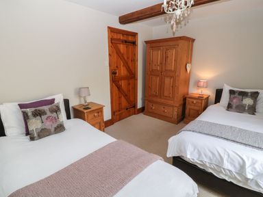 A bedroom with two single beds wooden furniture and a wooden door at Hazel Barn in North Molton