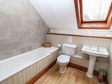 A bathroom with a bathtub, toilet, pedestal sink, and a skylight window at Hazel Barn in North Molton