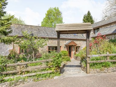 A stone cottage with a wooden archway and garden in front at Hazel Barn in North Molton