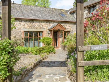 A stone cottage with a pathway and garden plants at Hazel Barn in North Molton