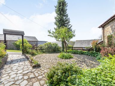 An outdoor garden area with a stone pathway a small tree and surrounding plants near stone buildings at Hazel Barn in North Molton