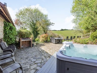 An outdoor patio with a hot tub stone flooring dining table and chairs and a brick barbecue at Hazel Barn in North Molton