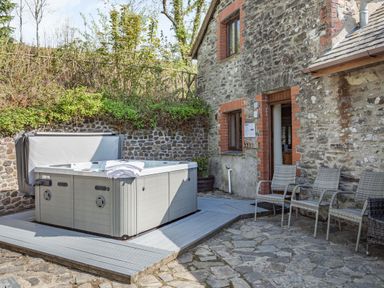 An outdoor patio area with a hot tub towels on it three chairs against a stone wall at Hazel Barn in North Molton