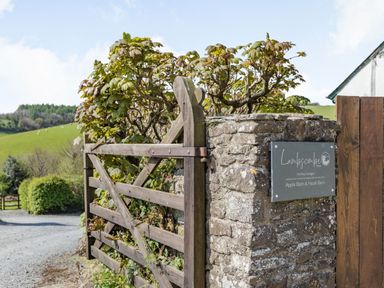 A wooden gate next to a stone pillar with a sign for holiday cottages at Lambscombe Farm in North Molton