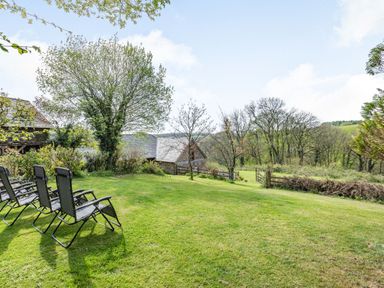 A grassy garden area with four reclining chairs near trees and a wooden fence at Hazel Barn in North Molton