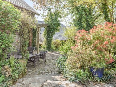 A stone patio with garden chairs and a table surrounded by plants and trees at Hazel Barn in North Molton