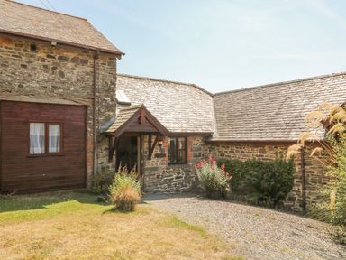 An exterior view of a stone and wood cottage with a small porch and gravel path at Oak Cottage in North Molton