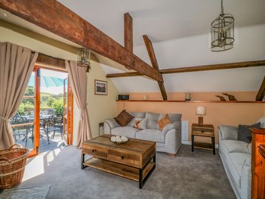 A living room with wooden beams two gray sofas a wooden coffee table and open French doors leading to an outdoor patio at Oak Cottage in North Molton