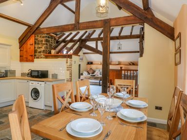 A kitchen and dining area with wooden table set for six and visible living room behind wooden beams at Oak Cottage in North Molton