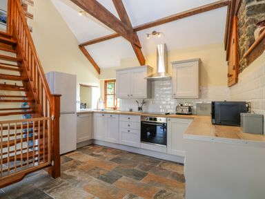 A kitchen with wooden stairs a refrigerator white cabinets and tiled floor at Oak Cottage in North Molton